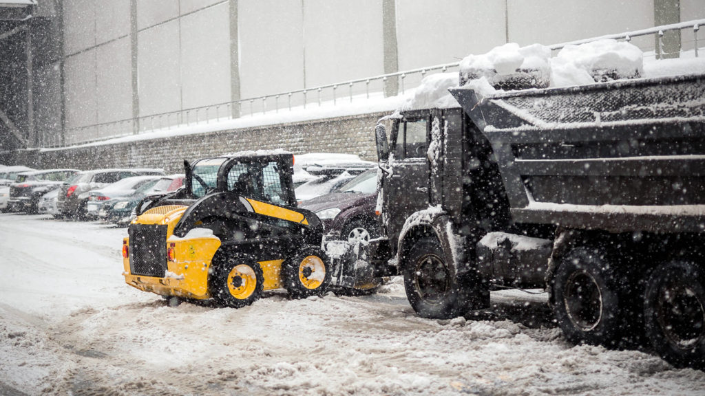 A bobcat loading removed snow into a dump truck.