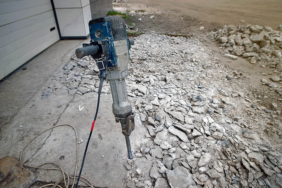 A jackhammer being used to break up a concrete driveway.