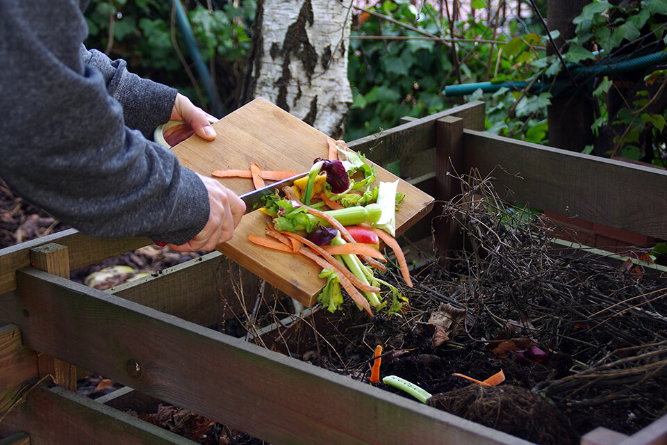 Adding kitchen scraps into a compost bin.