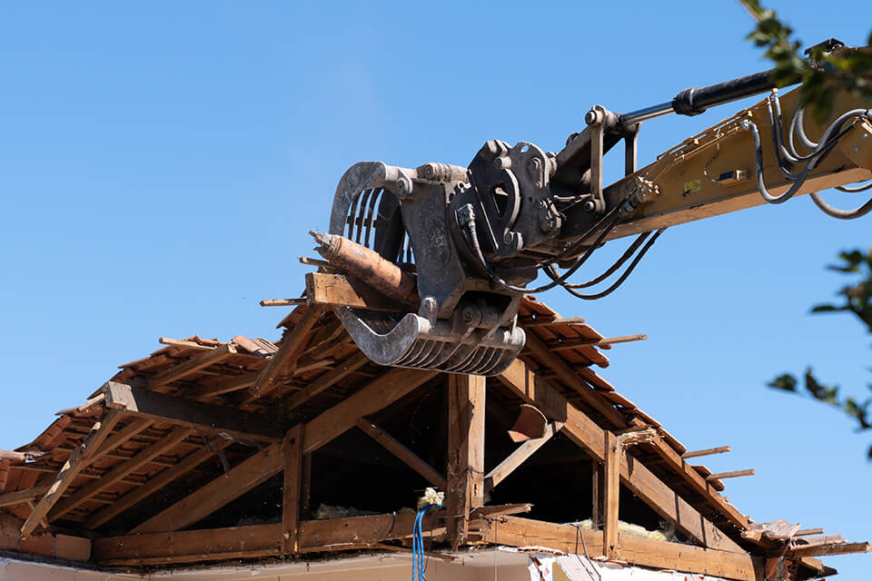 An excavator demolishing the roof of a house.