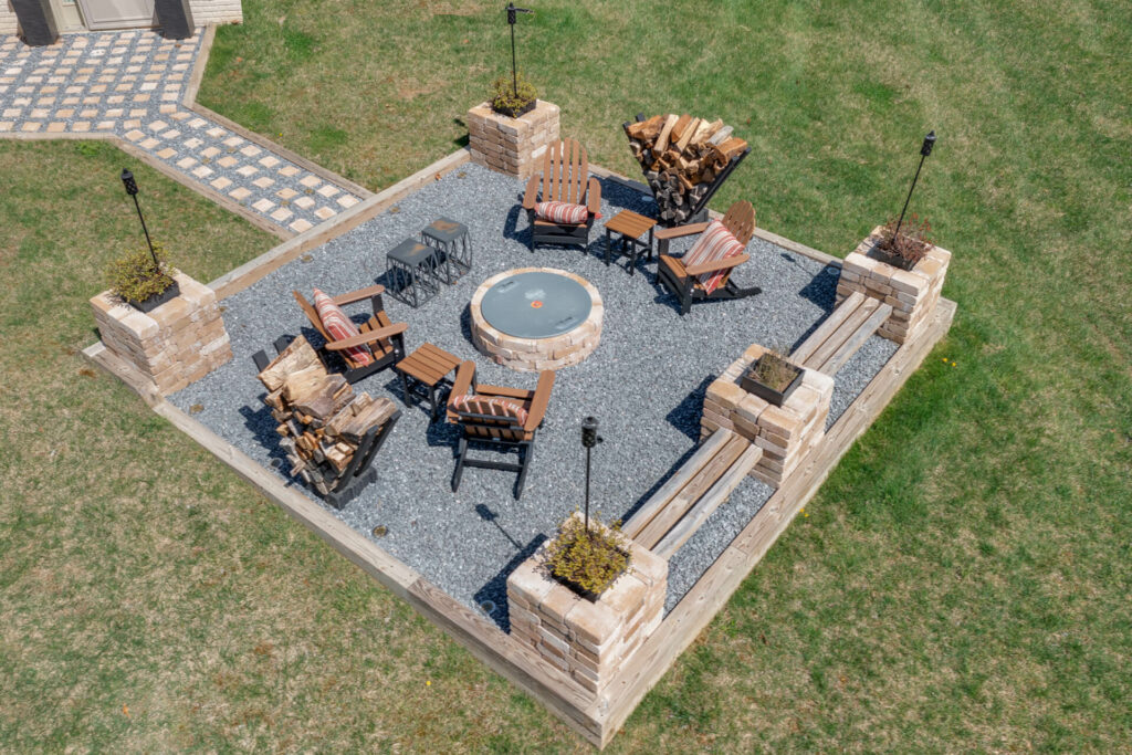 A rustic gravel patio with fire pit and benches made of bricks and timber.